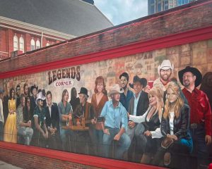 Colorful mural of Dolly Parton wearing her signature rhinestone-studded outfit and big blonde hair on a Nashville street wall.